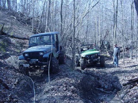 1992 Ford Bronco - Two off-road Jeeps tackle a challenging trail through a dense forest.