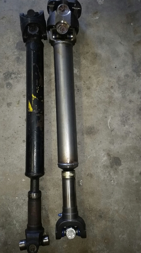 1968 Ford Bronco - Two driveshafts are shown side-by-side on a concrete floor. The driveshaft on the left is black and appears older, while the driveshaft on…