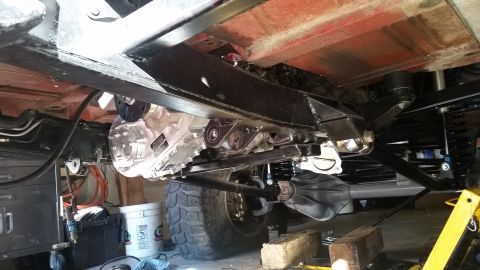 1968 Ford Bronco - The underside of a vehicle shows a custom transfer case modification with a silver aluminum housing, mounted to the frame. Visible suspensi…