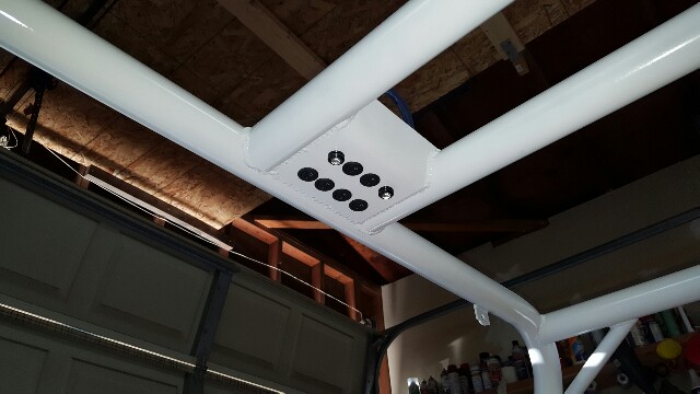White roll cage with a central plate and eight black bolts in a garage.
