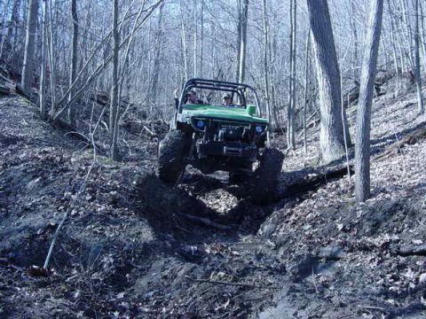1992 Ford Bronco - This off-road vehicle navigates a challenging, muddy incline surrounded by trees.