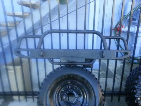 1968 Ford Bronco - A custom steel aftermarket front bumper is mounted on a vehicle, with a tire visible in the foreground. The bumper has a rugged, utilitaria…