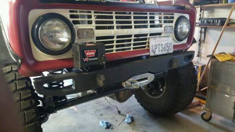 1968 Ford Bronco - Front view of a red and white 1968 Ford Bronco with a black aftermarket bumper and a WARN VR10,000 winch mounted on the front. The vehicle…
