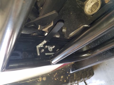 1968 Ford Bronco - A close-up, low-angle view shows the underside of a vehicle seat, focusing on a black seat adjustment lever mechanism with a silver bracket…