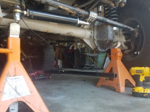 1968 Ford Bronco - The underside of a vehicle is supported by jack stands, with a black steering stabilizer and a differential visible. A yellow power drill r…