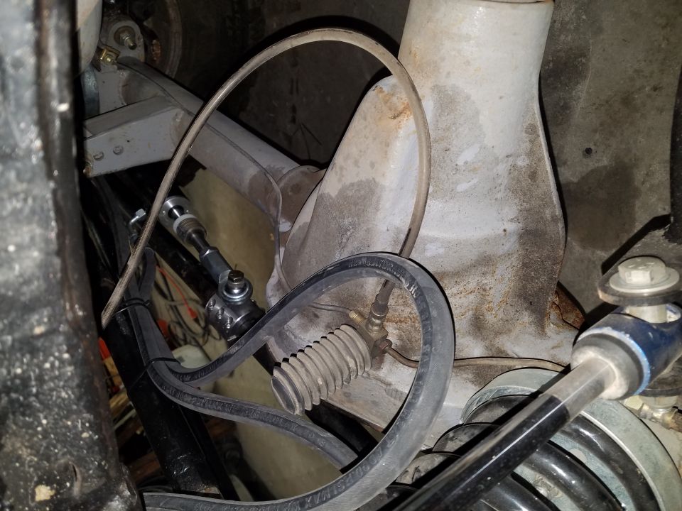 Close-up of vehicle suspension and steering components, including tie rod, brake line, and coil spring.