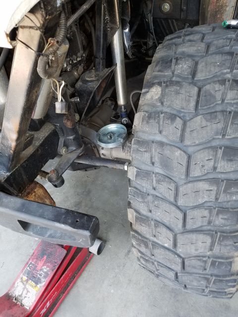 1968 Ford Bronco - A close-up view of the front suspension and tire of a vehicle, possibly a 1968 Ford Bronco, with a red hydraulic jack visible underneath th…