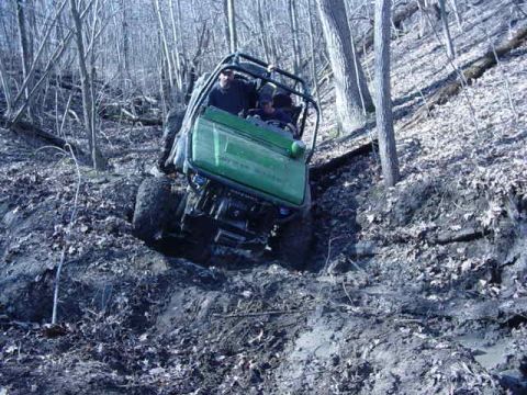 1992 Ford Bronco - A green off-road vehicle navigates a steep, muddy incline surrounded by trees.