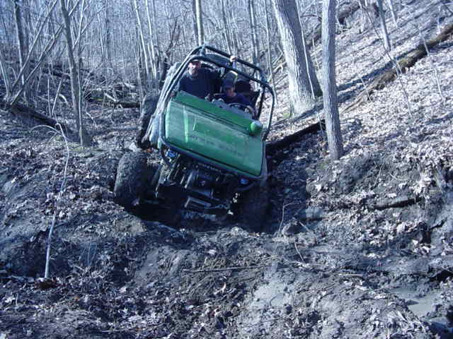 Green off-road vehicle climbing a muddy hill in a wooded area