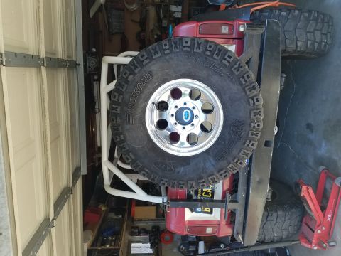 1968 Ford Bronco - A red off-road vehicle, likely a Ford Bronco, is parked in a garage with a large spare tire mounted on the rear. A white roll cage is visib…