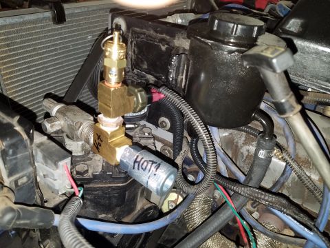 1968 Ford Bronco - A close-up view of an engine bay shows a brass fitting with "HOT!" written on it, connected to various hoses and wires. A black power steer…