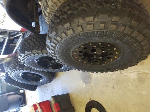 1968 Ford Bronco - A close-up, low-angle view of four large off-road tires and custom black beadlock wheels mounted on a vehicle, possibly a Ford Bronco, rest…