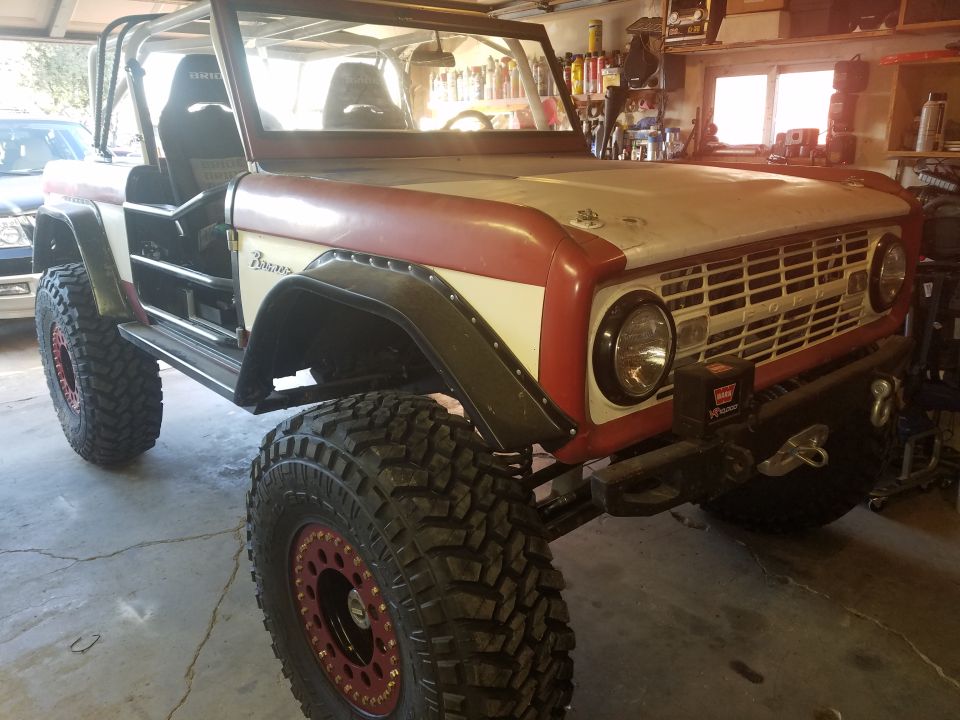 Custom 1968 Ford Bronco with off-road tires and roll cage in a garage.