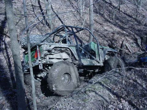 1992 Ford Bronco - This heavily modified off-road vehicle is deeply stuck in mud on a wooded trail.
