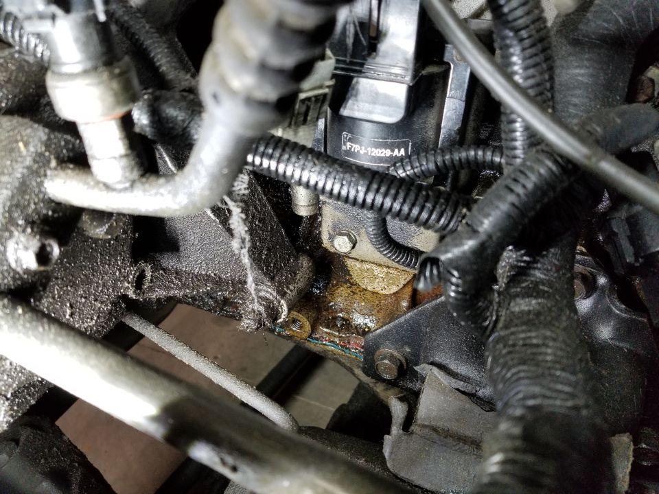 Ford coil pack marked F7PJ-12029-AA above an oily engine block and head joint