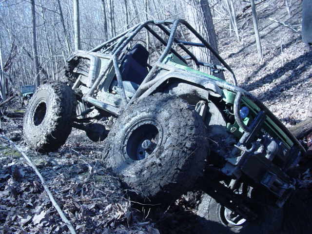 Muddy off-road buggy with roll cage stuck in woods