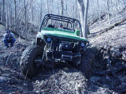 1992 Ford Bronco - Off-road vehicle navigates a challenging muddy hill in a forest setting.
