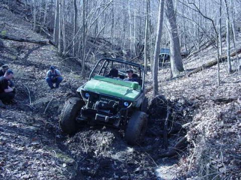 1992 Ford Bronco - An off-road buggy navigates a muddy, wooded terrain with onlookers observing the challenge.