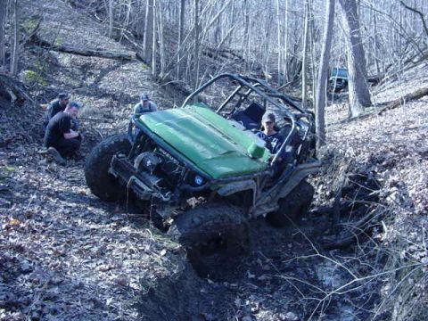 1992 Ford Bronco - An off-road vehicle navigates a muddy, wooded terrain with several people nearby.