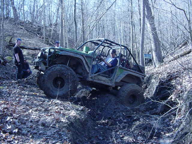 Off-road vehicle with roll cage climbing a muddy hill, another vehicle visible in background