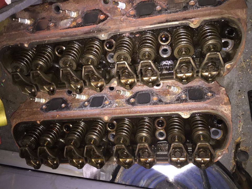 Overhead view of two V8 engine cylinder heads with visible spark plugs, rocker arms, and valve springs.