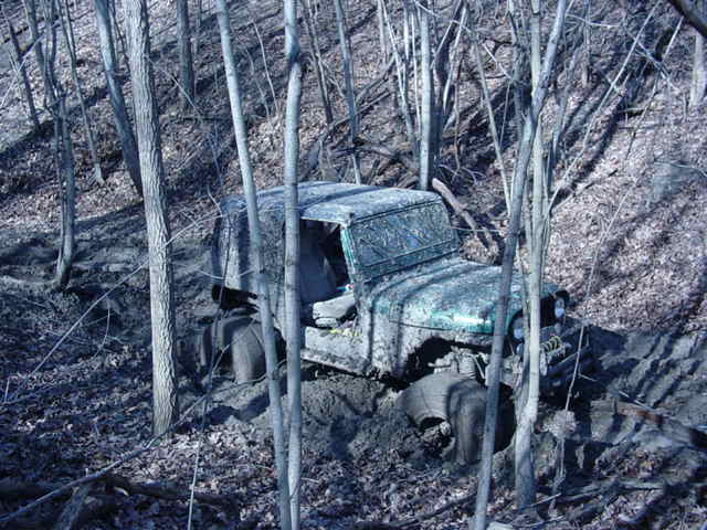Mud-covered off-road vehicle stuck in a wooded area with trees and mud all around
