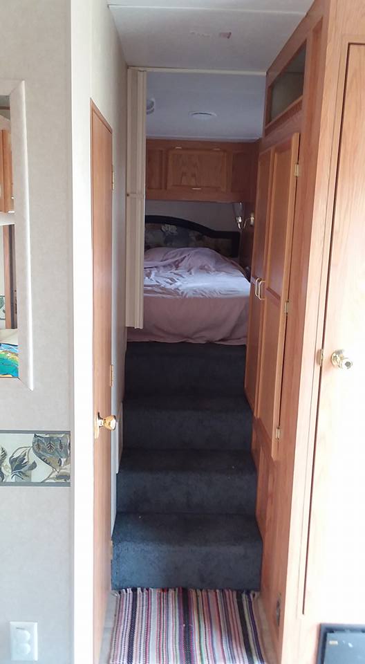 Interior of an RV with stairs leading to a bedroom and a wooden closet.