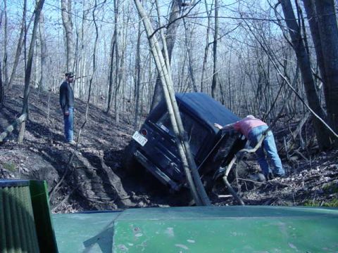 1992 Ford Bronco - A 1992 Ford Bronco is stuck on a steep, wooded incline with two individuals nearby.