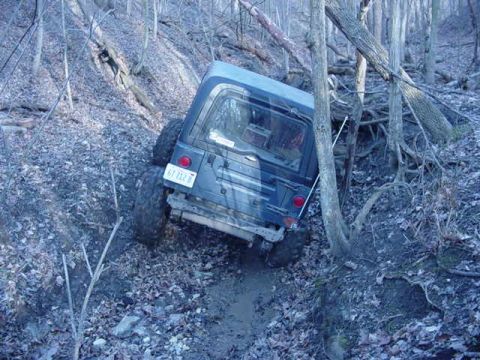 1992 Ford Bronco - Jeep Wrangler TJ navigating a steep, muddy, off-road trail through a dense forest.