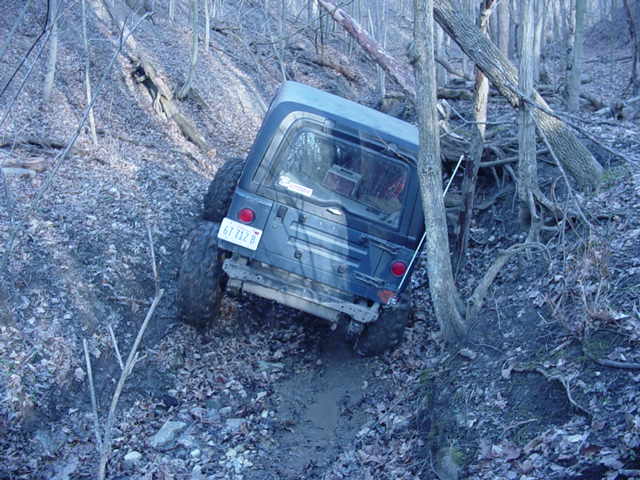 Jeep Wrangler TJ tilted on a muddy, wooded trail. License plate reads 67 712 B