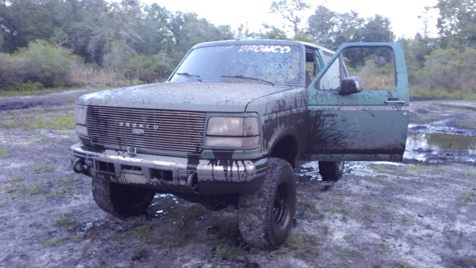 Muddy 1996 Ford Bronco with driver's door open, "BRONCO" on windshield.
