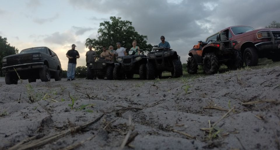 Group of people with off-road vehicles including a black SUV and ATVs.