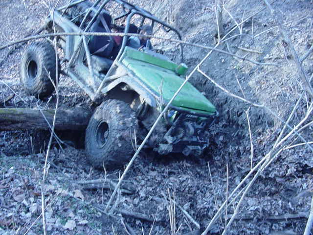 Green off-road vehicle with roll cage tilted on a muddy incline