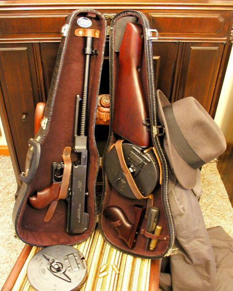 1992 Ford Bronco - A violin case is open, revealing a Thompson submachine gun, a drum magazine, a fedora hat, and other accessories. The case is placed on a s…