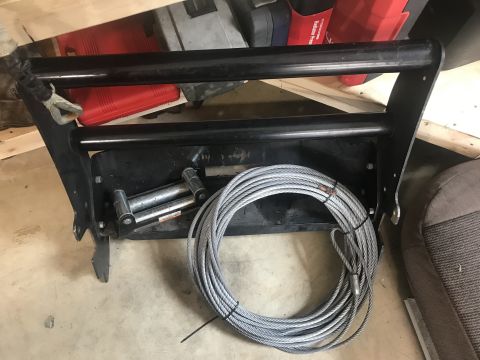 1989 Ford Bronco - A black metal winch mount with a coiled steel cable is shown in a garage setting. The mount has two horizontal bars and a winch drum visibl…
