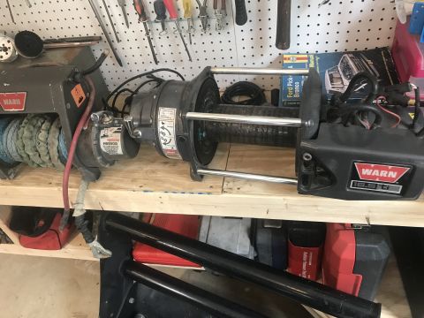 1989 Ford Bronco - Two Warn winches are mounted on a wooden shelf, with a Ford Bronco manual visible behind them. The winches are connected by cables and have…