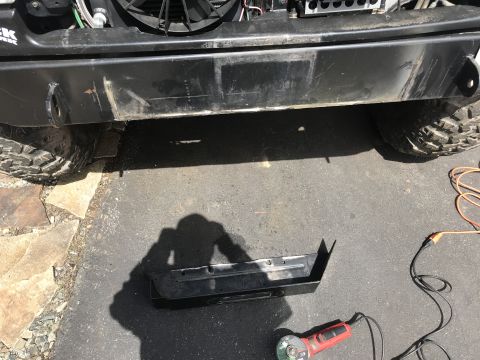 1989 Ford Bronco - A black aftermarket bumper is shown mounted on the front of a vehicle, with a black metal bracket and a red angle grinder on the asphalt be…