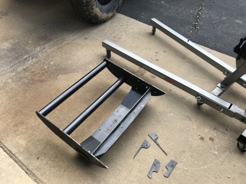 1989 Ford Bronco - A black metal frame with two horizontal bars sits on a concrete surface next to a silver engine hoist. Several small metal brackets are sca…