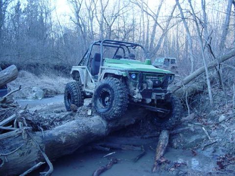 1992 Ford Bronco - A modified Suzuki Samurai navigates a challenging off-road course, crossing a large fallen log.