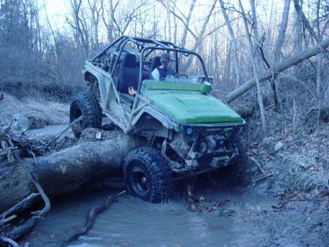 1992 Ford Bronco - Modified off-road vehicle navigates a challenging muddy path surrounded by trees.