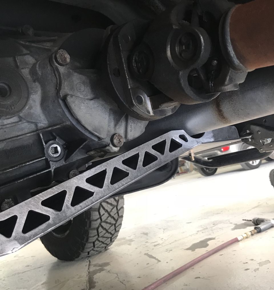 Underneath view of vehicle drivetrain with custom brace and tire.