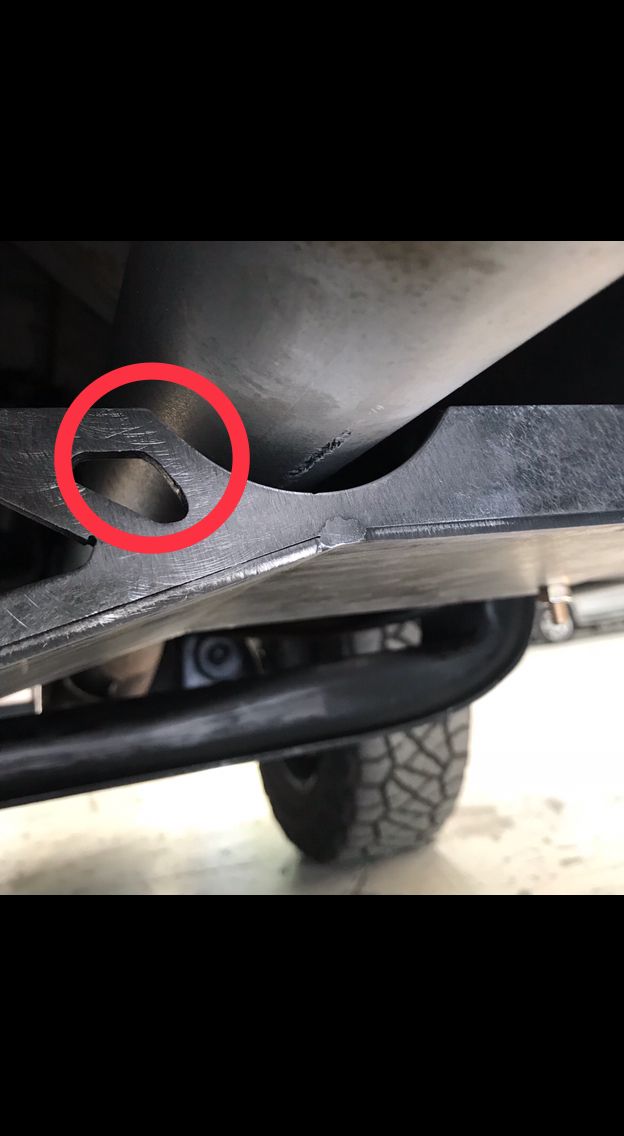 Undercarriage of a vehicle with a red circle around a cutout on a metal component. Tire visible.