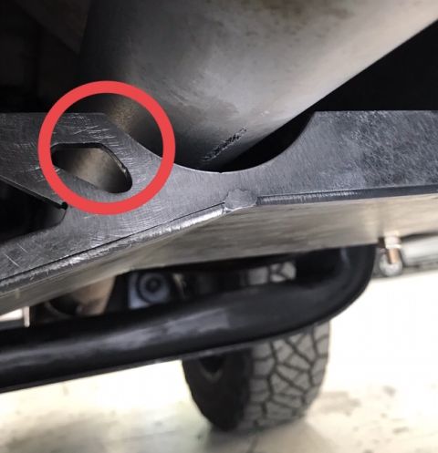 1995 Ford Bronco - A close-up view of the underside of a vehicle, focusing on a metal skid plate with a red circle highlighting a cut-out section. The skid pl…