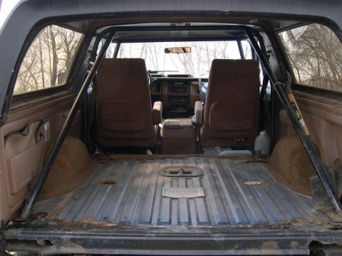 1986 Ford Bronco - The interior of a 1986 Ford Bronco, viewed from the bed, reveals its seats and a roll cage.