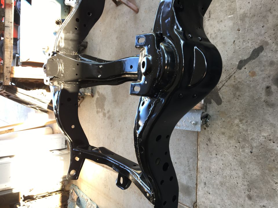 Black painted car chassis frame on concrete floor.