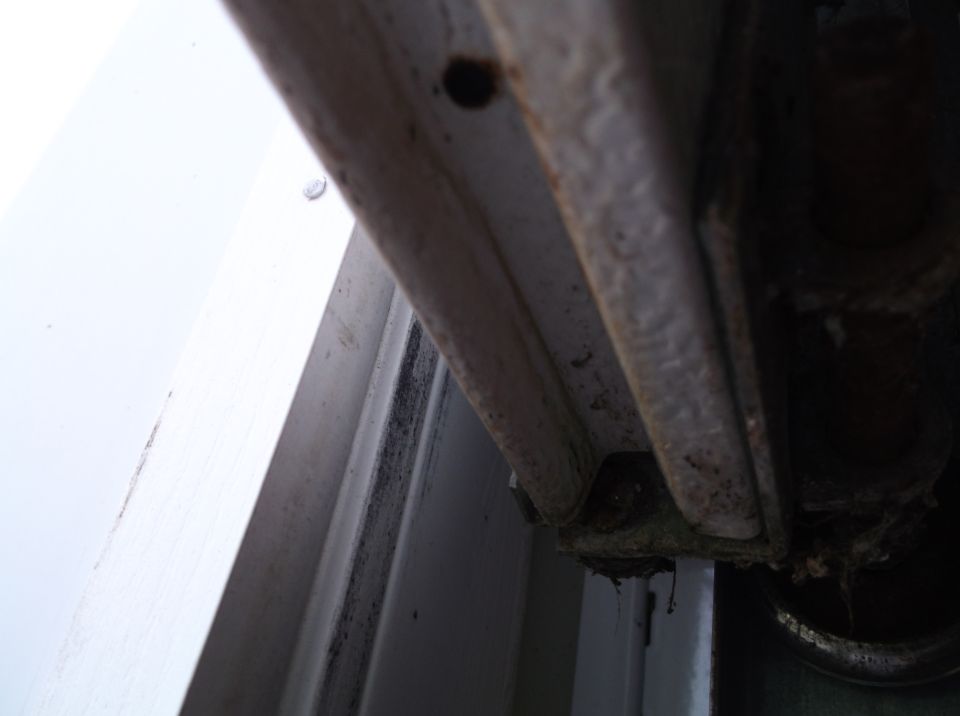 Close-up of rusted metal frame with black mold on white door frame.