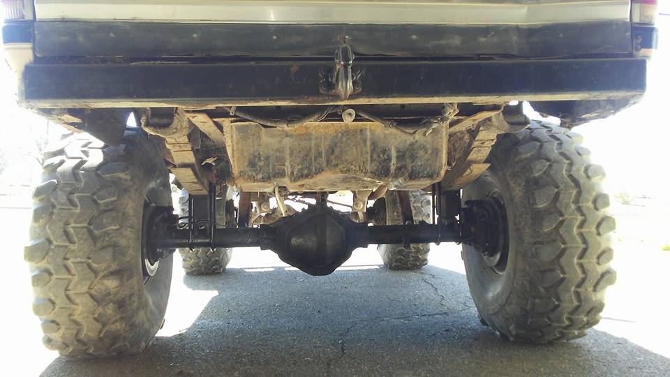 Underside of a lifted vehicle showing rear differential, leaf springs, and large off-road tires.