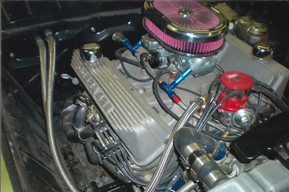 Modified V8 engine with 'COBRA 428' valve cover, Holley carb, pink air filter, and red MSD distributor.