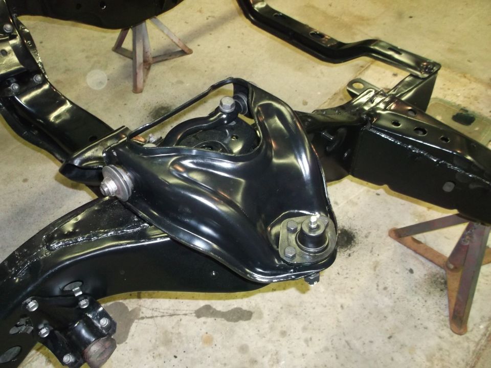 Black painted automotive suspension subframe assembly with control arms and ball joints.