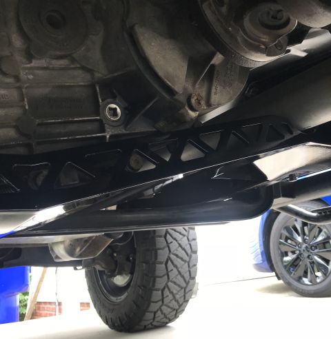 1995 Ford Bronco - Underside view of a black aftermarket skid plate with a triangular cut-out pattern, mounted beneath the transmission or transfer case of a…